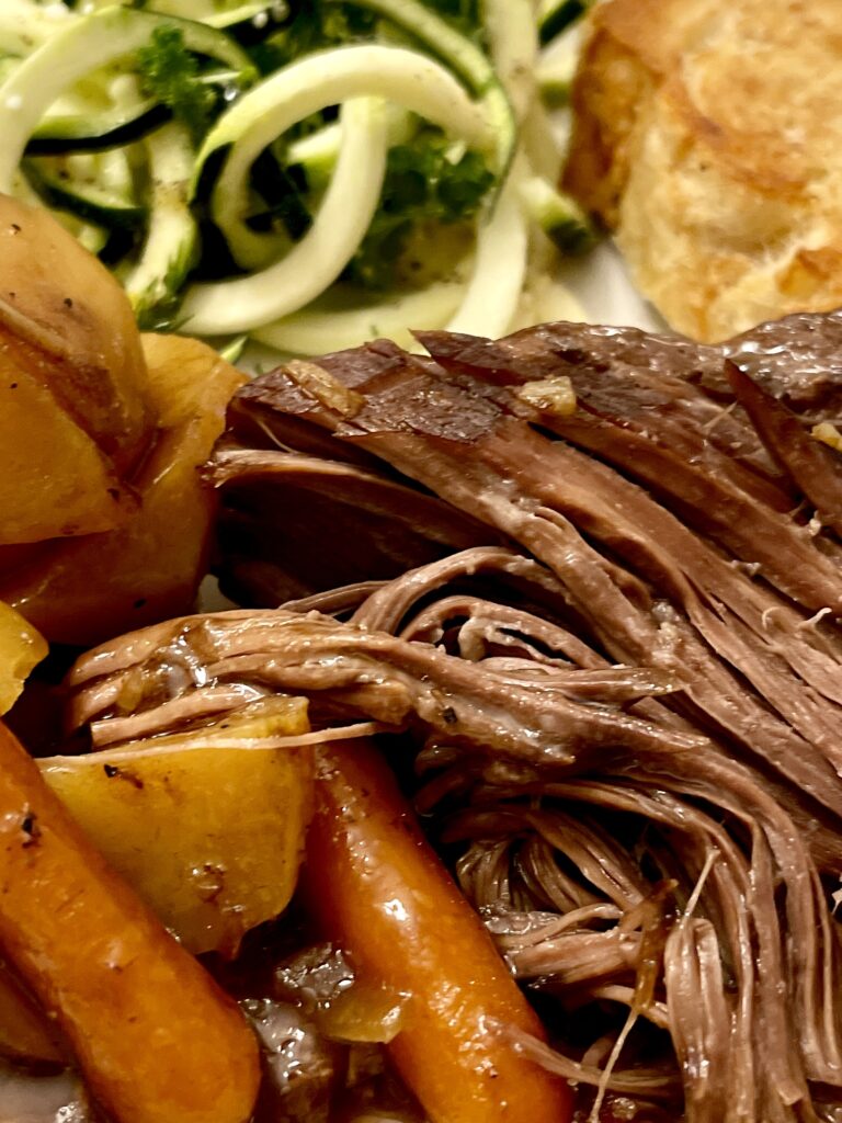 close up of a plate with roast beef, potatoes, carrots, bread and zucchini salad