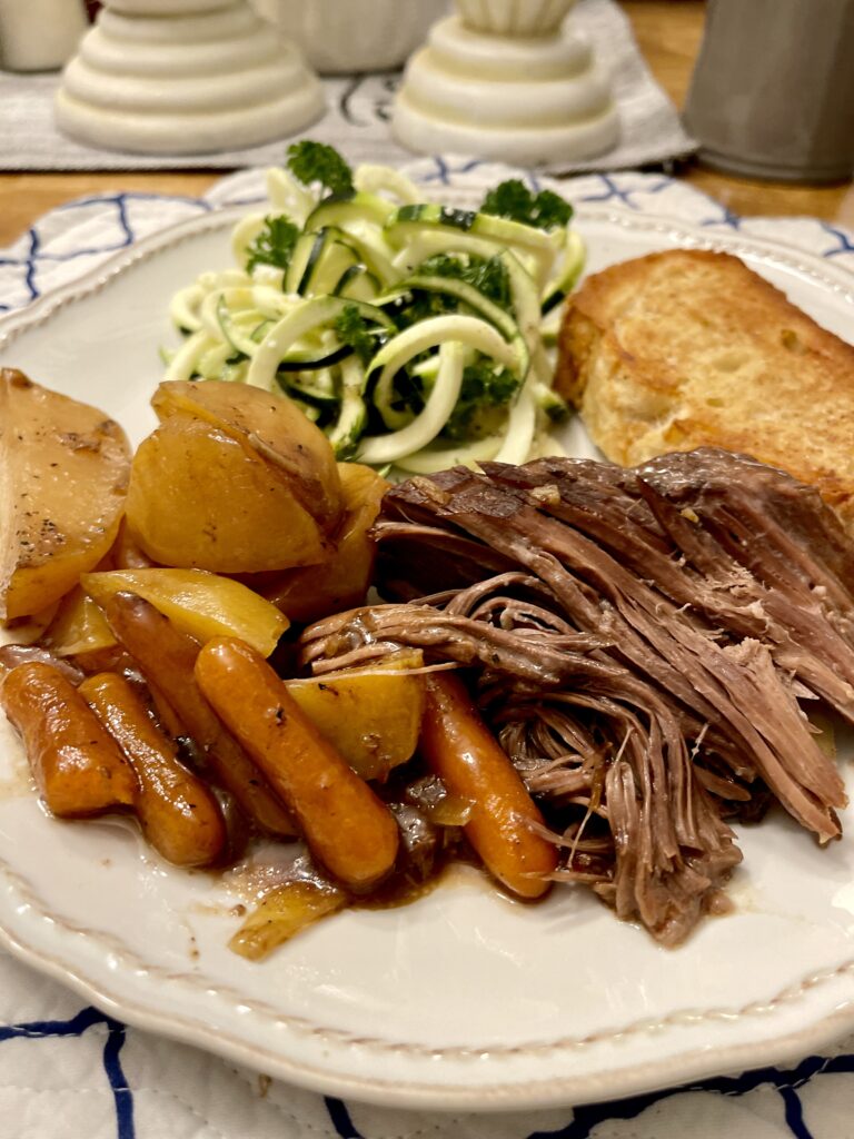 plate with roast beef, potatoes, carrots, crusty bread and a zucchini lemon salad.