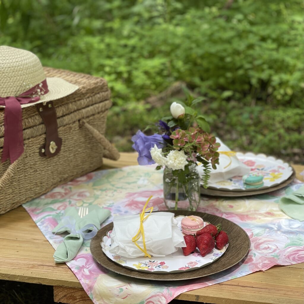 picnic table set up with picnic basket, plates, hat and centerpiece of perennials