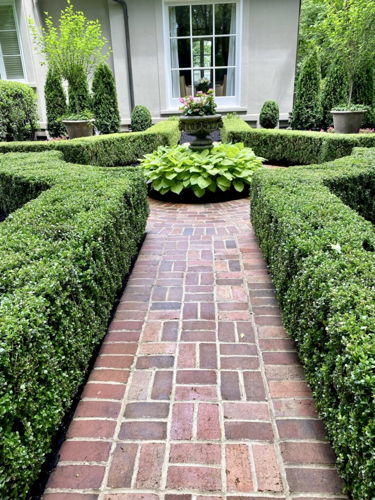 Formal garden with brick sidewalk, boxwood, and centerpiece in circle surrounded by hosta.