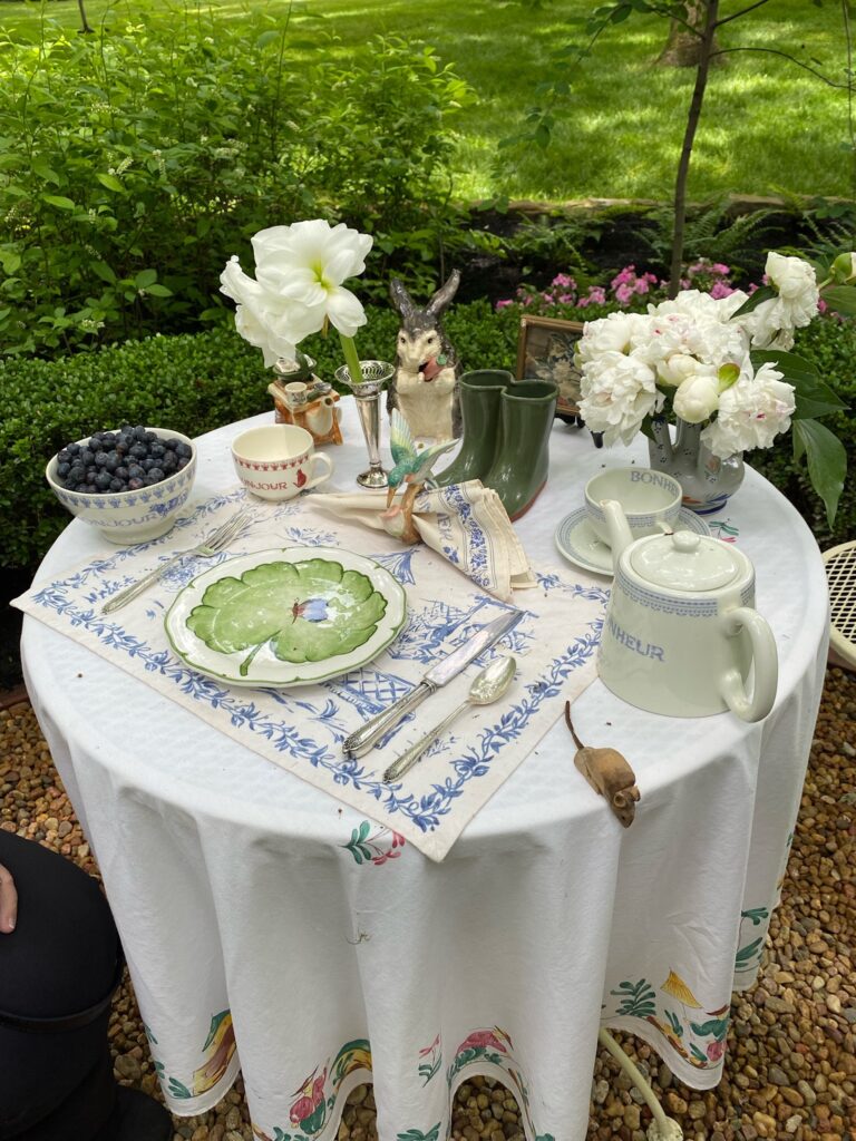 round skirted table in garden set with tea set, place setting, fresh peonies, and fruit