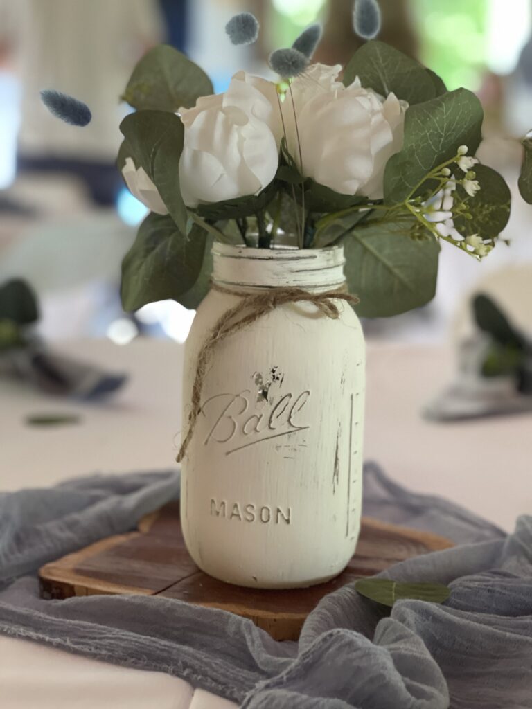 painted white jars with silk flowers on wooden slabs centerpieces