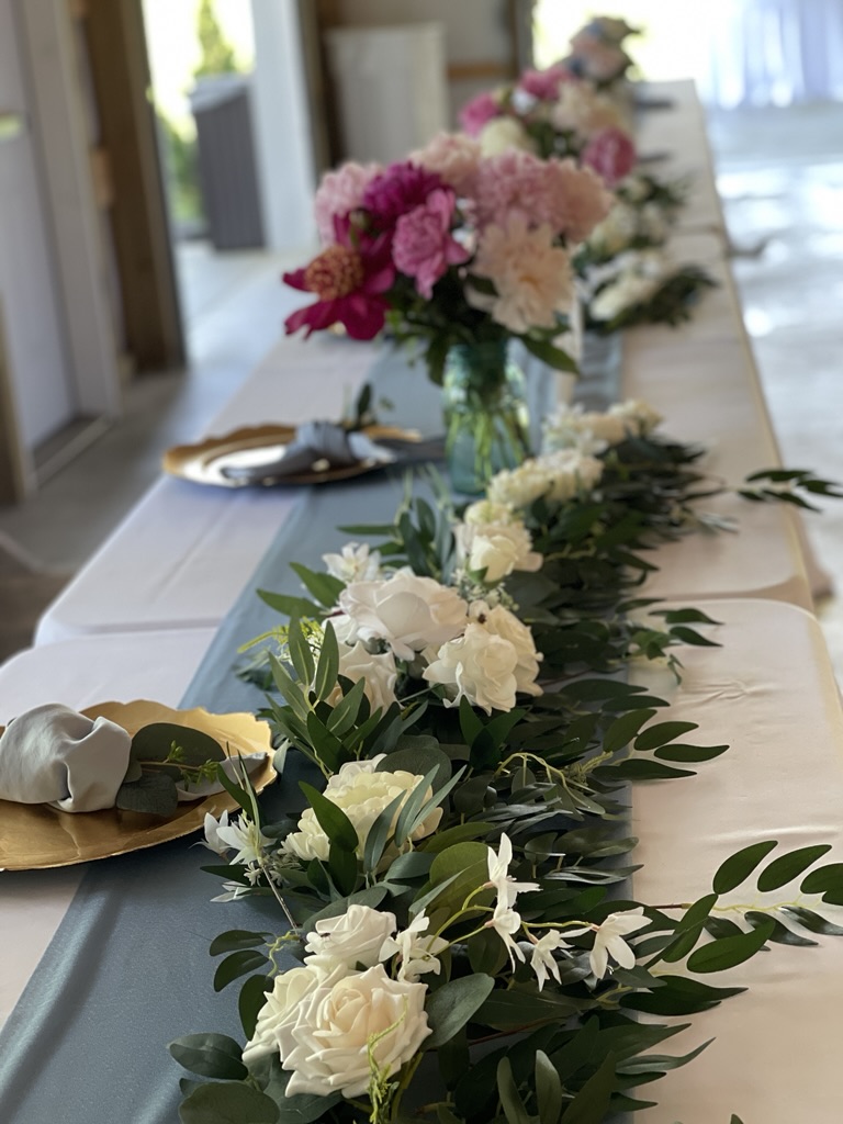 wedding table set with white and pink silk peonies and place settings with a blue runner on the table