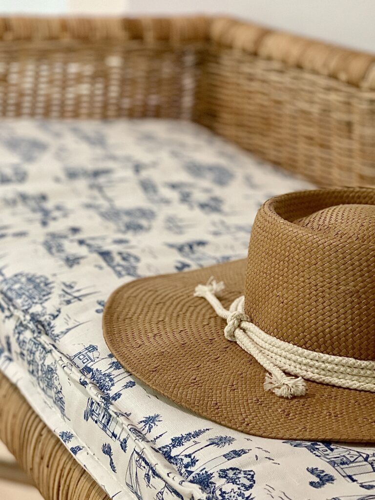 hat on a blue toile covered pad on a willow bench