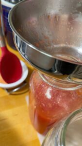 funnel in canning jar adding tomato juice