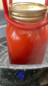 lifting jar of homemade tomato juice into canner