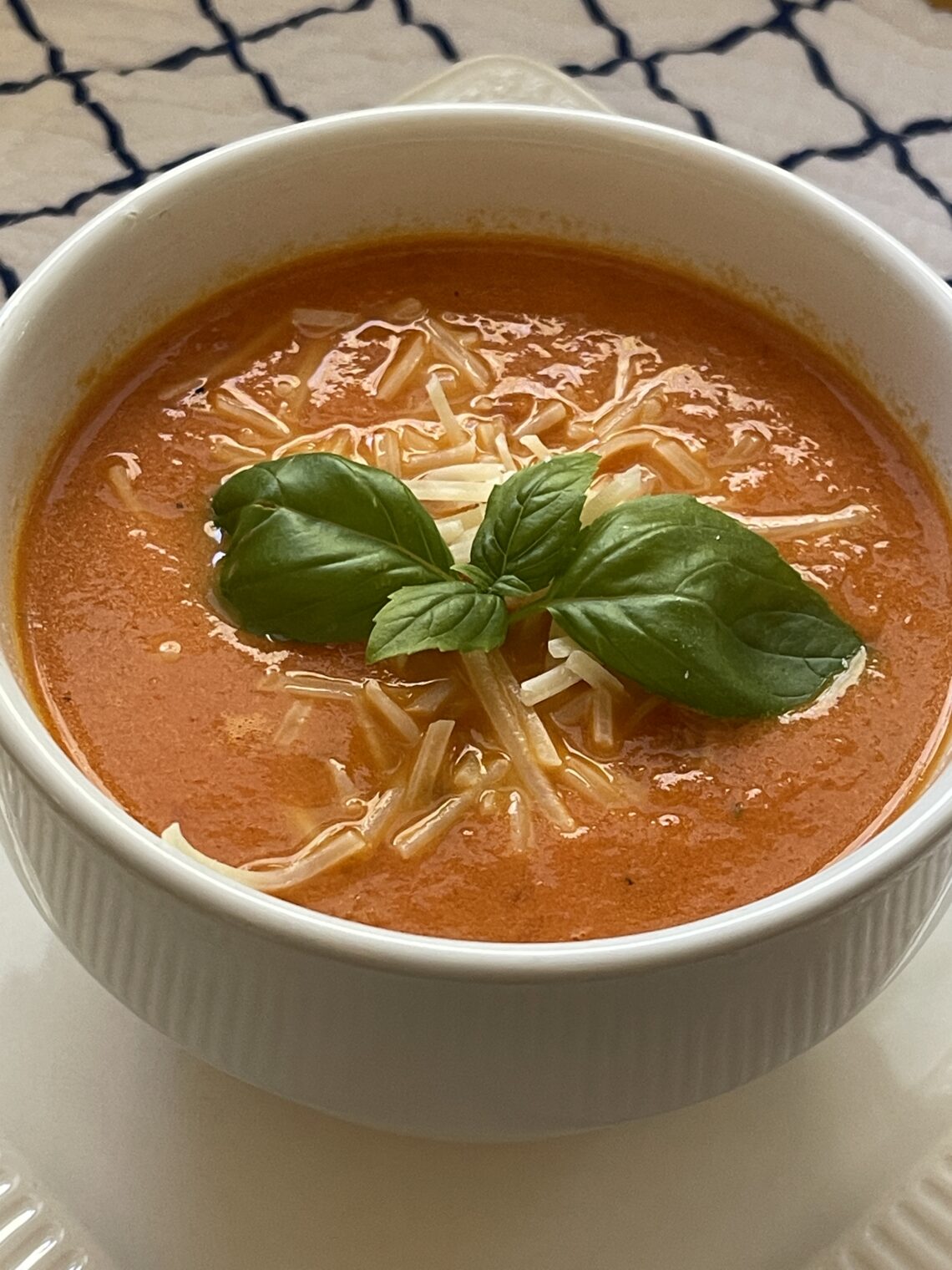 tomato basil soup in bowl with Parmesan cheese and fresh basil