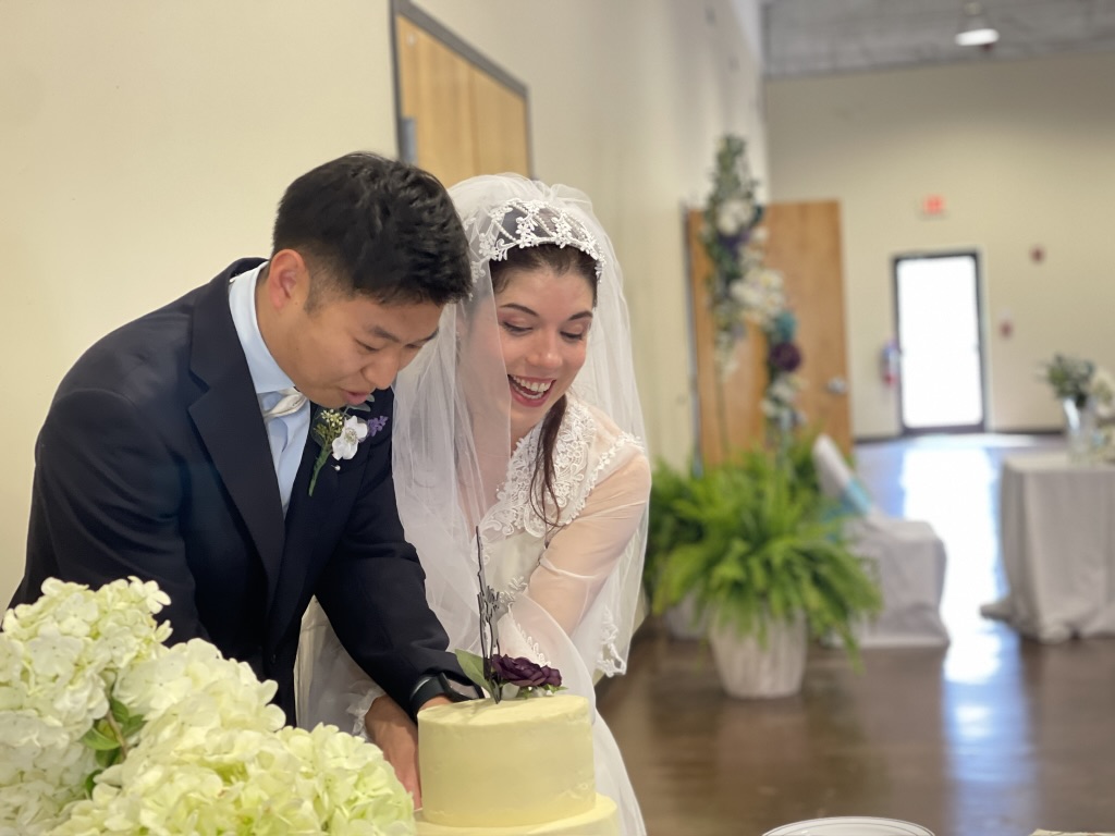 cutting the wedding cake with bride smiling