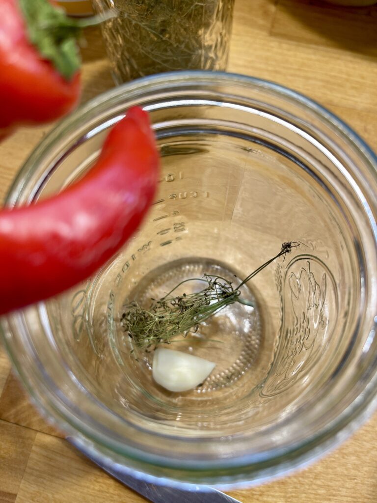 adding garlic, dill and red pepper to pickled okra jars