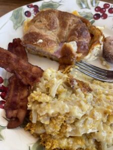 plate with croissant breakfast sandwich, bacon, muffin and potato casserole