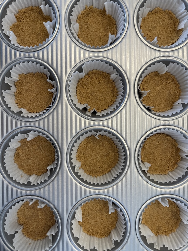 muffin pan filled with liners and graham cracker crusts