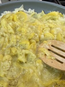 Pressing cooked summer yellow squash with back of wooden spoon to mash