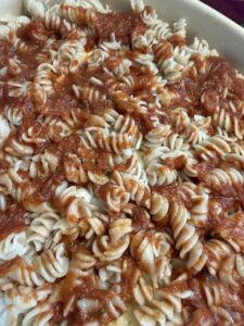 cooked rotini in a greased casserole dish with sauce added to top