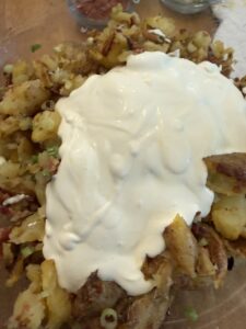 adding dressing, green onions, and bacon to smashed potato salad