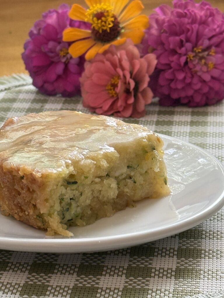 piece of glazed zucchini cake with zinnias behind